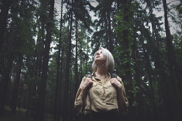 Mujer rubia con mochila en día lluvioso en bosque