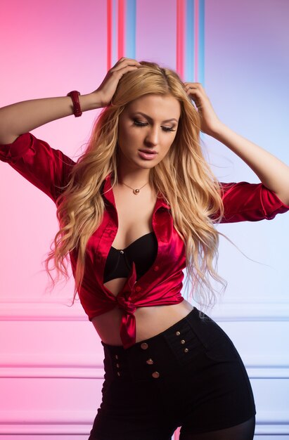 Mujer rubia de moda con pelo largo ondulado posando en el estudio en blusa de seda roja