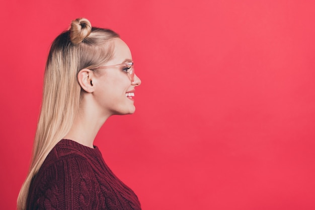 Mujer rubia con moños y gafas posando contra la pared roja