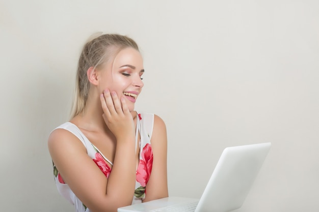 Mujer rubia muy alegre mirando a la computadora portátil, posando sobre el fondo gris