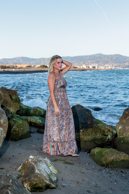 mujer rubia muy bonita en vestido posando en la playa con el mar en el fondo