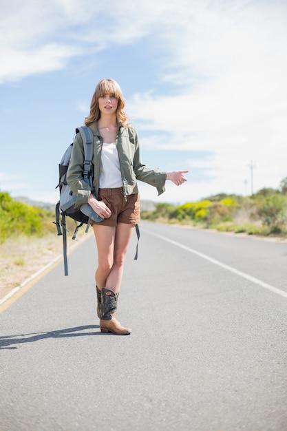 Mujer rubia natural que presenta mientras que hace autostop