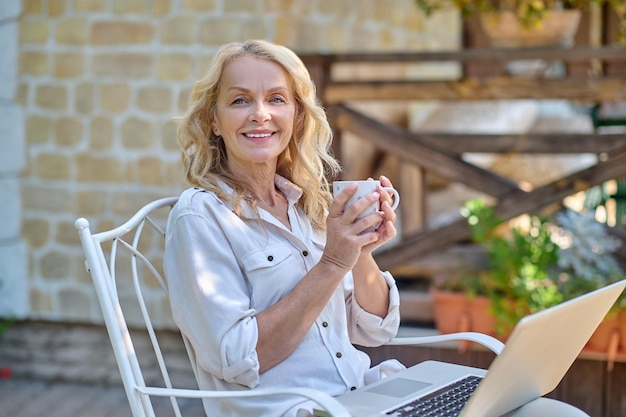 Mujer rubia navegando por internet mientras toma su café matutino