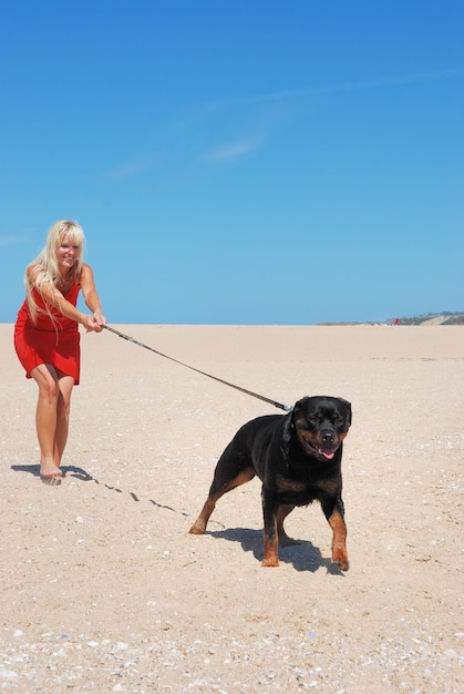 Mujer rubia paseando a su perro en la playa