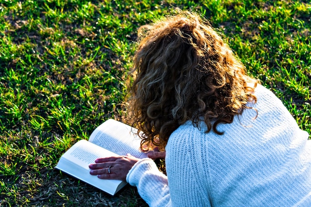 Foto mujer rubia y de pelo rizado leyendo en el parque.