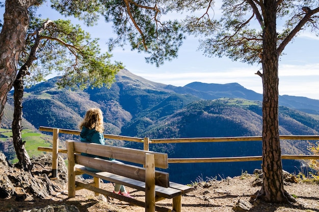 Mujer rubia con el pelo rizado sentada en un banco mirando las vistas de las montañas de Ribes girona