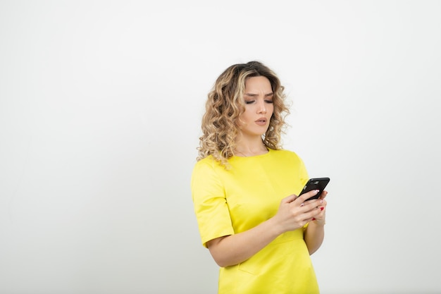 mujer rubia de pelo rizado en vestido amarillo comprobando su teléfono celular.