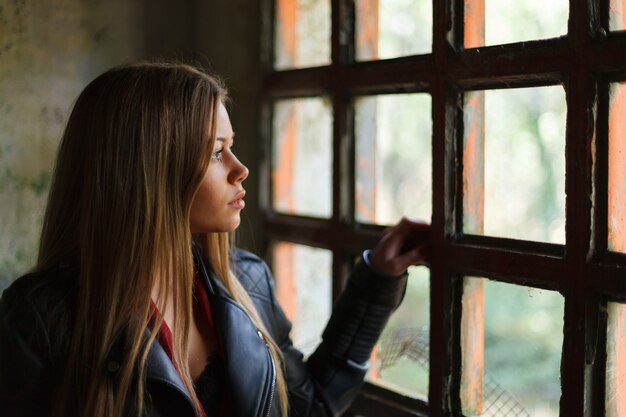 Foto mujer rubia pensativa junto a una ventana vintage