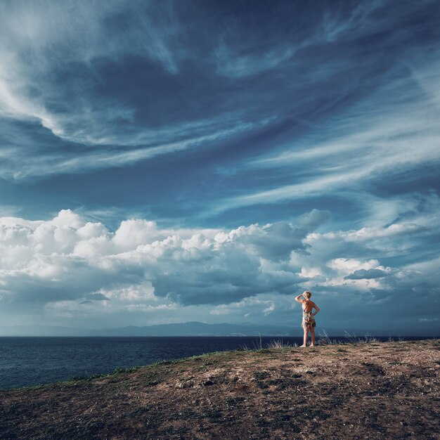 Mujer rubia de pie en la cima de la colina y mirando al mar Hermoso cielo sobre el mar Egeo