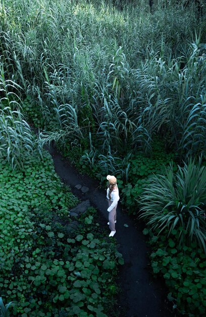 Mujer rubia de pie rodeada de plantas en el medio de la naturaleza