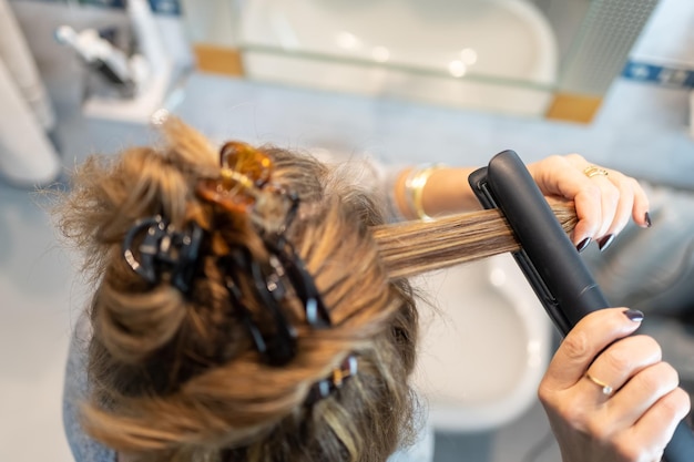 Mujer rubia planchando su cabello con un electrodoméstico en la vista superior del baño