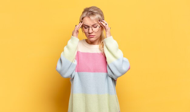 Mujer rubia que parece concentrada, pensativa e inspirada, haciendo una lluvia de ideas e imaginando con las manos en la frente