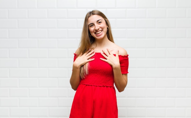 Mujer rubia que parece feliz, sorprendida, orgullosa y emocionada, apuntando a sí misma