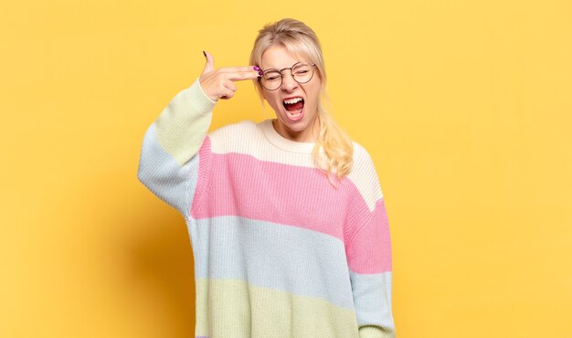 Mujer rubia que parece infeliz y estresada, gesto de suicidio haciendo un signo de pistola con la mano, apuntando a la cabeza