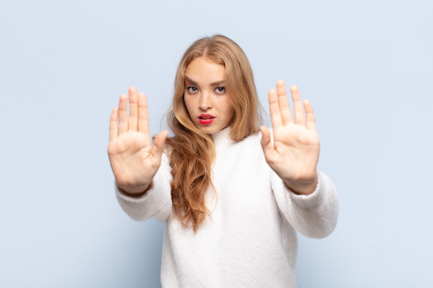 Mujer rubia que parece seria, infeliz, enojada y disgustada prohibiendo la entrada o diciendo que pare con ambas palmas abiertas