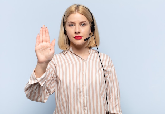 Mujer rubia que parece seria, severa, disgustada y enojada mostrando la palma abierta haciendo gesto de parada