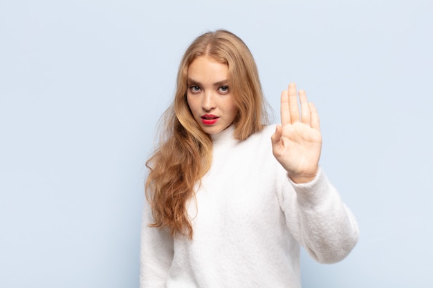 Mujer rubia que parece seria, severa, disgustada y enojada mostrando la palma abierta haciendo gesto de parada