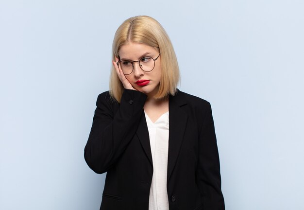 Mujer rubia que se siente aburrida, frustrada y con sueño después de una tarea tediosa, aburrida y tediosa, sosteniendo la cara con la mano