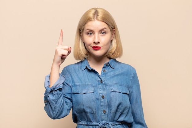 Mujer rubia que se siente como un genio levantando el dedo con orgullo en el aire después de darse cuenta de una gran idea, diciendo eureka