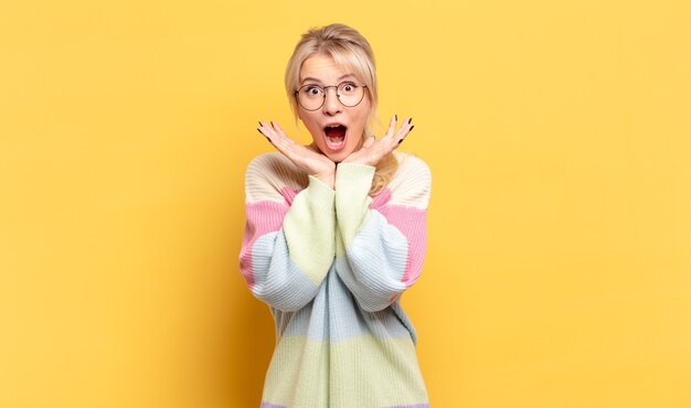 Mujer rubia que se siente conmocionada y emocionada, riendo, asombrada y feliz por una sorpresa inesperada.