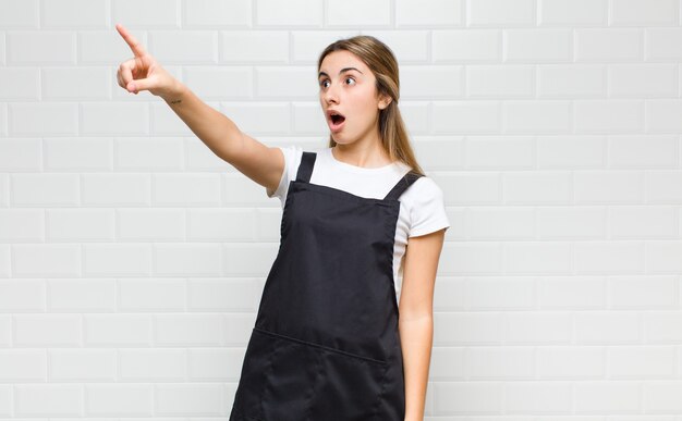 Foto mujer rubia que se siente conmocionada y sorprendida, apuntando y mirando hacia arriba con asombro con una mirada asombrada y con la boca abierta.