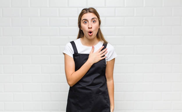 Mujer rubia que se siente conmocionada y sorprendida, sonriendo, tomando la mano al corazón, feliz de ser la indicada o mostrando gratitud