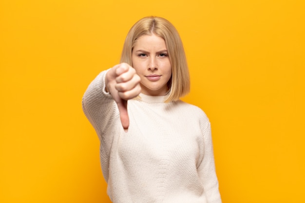 Mujer rubia que se siente enfadada, enojada, molesta, decepcionada o disgustada, mostrando el pulgar hacia abajo con una mirada seria.