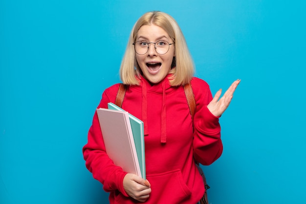 Mujer rubia que se siente feliz, emocionada, sorprendida o conmocionada, sonriendo y asombrada por algo increíble