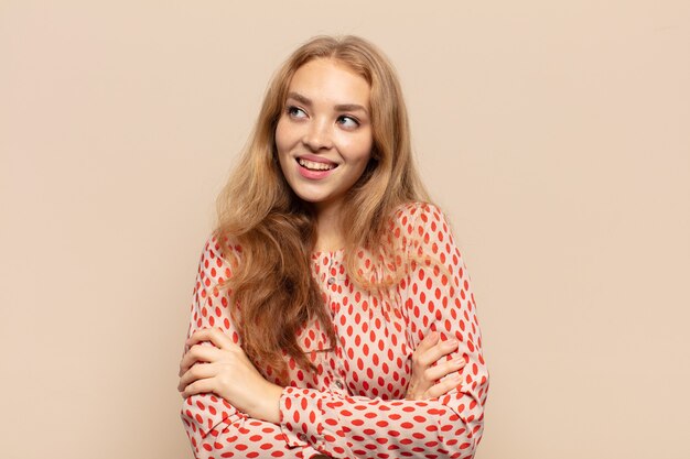 Mujer rubia que se siente feliz, orgullosa y esperanzada, preguntándose o pensando, mirando hacia arriba para copiar el espacio con los brazos cruzados