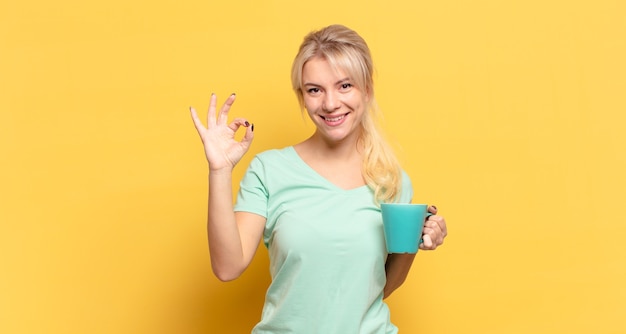 Mujer rubia que se siente feliz, relajada y satisfecha, mostrando aprobación con gesto bien, sonriendo