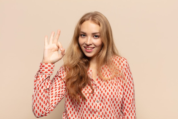 Mujer rubia que se siente feliz, relajada y satisfecha, mostrando aprobación con gesto bien, sonriendo