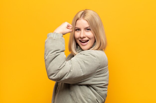 Mujer rubia que se siente feliz, satisfecha y poderosa, flexionando el ajuste y bíceps musculosos, luciendo fuerte después del gimnasio