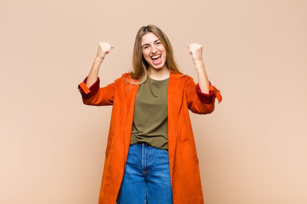 Mujer rubia que se siente feliz, sorprendida y orgullosa, gritando y celebrando el éxito con una gran sonrisa