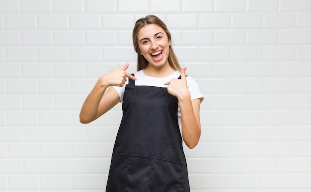 Mujer rubia que se siente feliz, sorprendida y orgullosa, señalando a sí misma con una mirada emocionada y asombrada