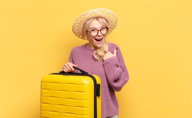 Mujer rubia que se siente feliz, sorprendida y orgullosa, señalando a sí misma con una mirada emocionada y asombrada