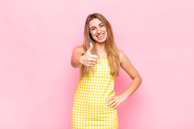 Mujer rubia que se siente orgullosa, despreocupada, segura y feliz, sonriendo positivamente con los pulgares hacia arriba