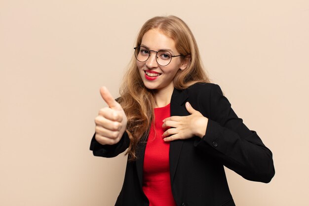 Mujer rubia que se siente orgullosa, despreocupada, segura y feliz, sonriendo positivamente con los pulgares hacia arriba