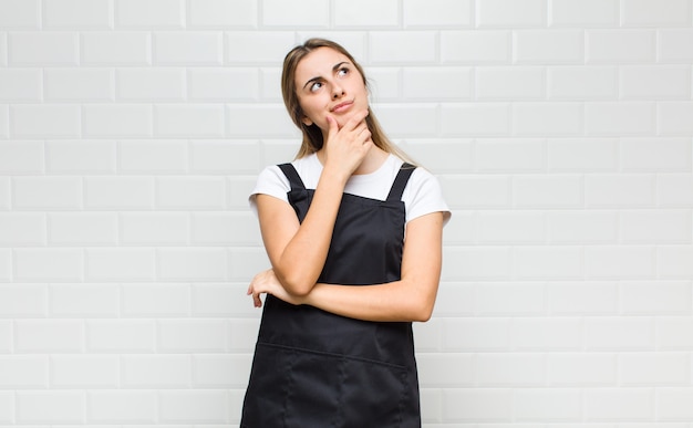 Mujer rubia que se siente pensativa, preguntándose o imaginando ideas, soñando despierto y mirando hacia arriba para copiar el espacio