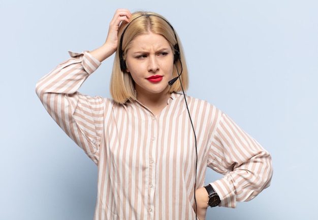 Mujer rubia que se siente perpleja y confundida rascándose la cabeza y mirando hacia un lado