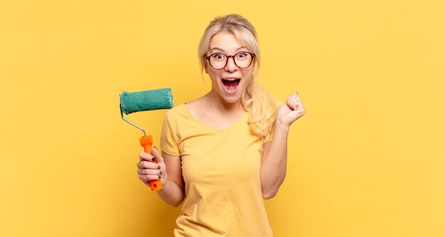 Mujer rubia que se siente sorprendida, emocionada y feliz, riendo y celebrando el éxito, diciendo ¡guau!