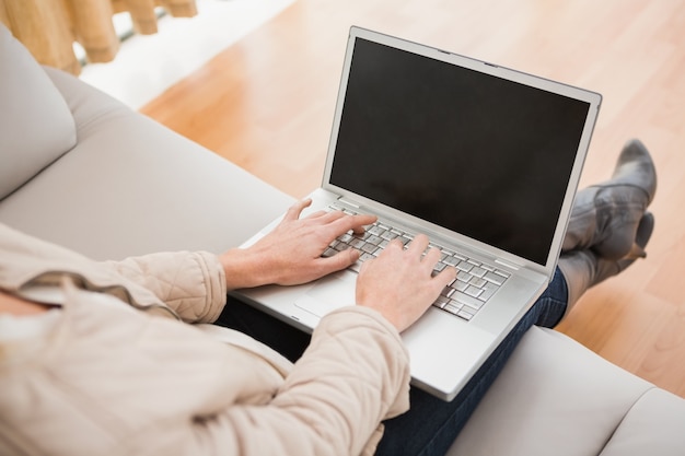 Mujer rubia que usa la computadora portátil en el sofá