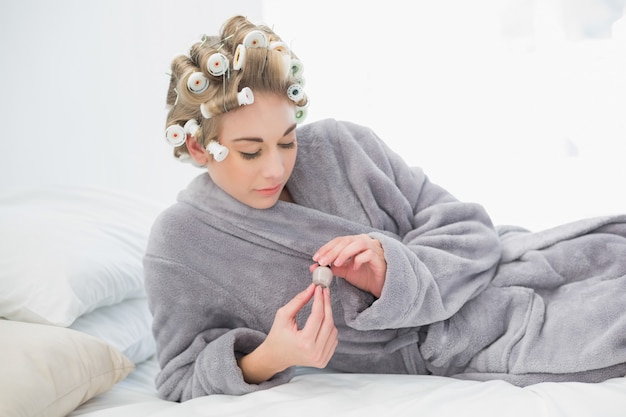 Mujer rubia relajada concentrada en rulos de pelo abriendo una olla de esmalte de uñas