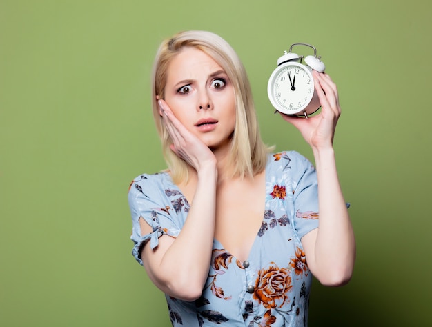 Mujer rubia con reloj despertador en pared verde