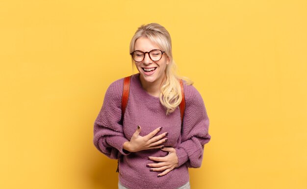 Mujer rubia riendo a carcajadas de una broma hilarante, sintiéndose feliz y alegre, divirtiéndose