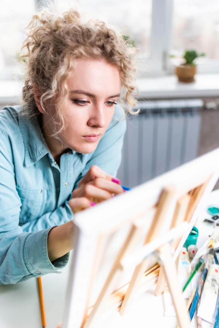 Foto mujer rubia rizada pintando un cuadro junto a la ventana