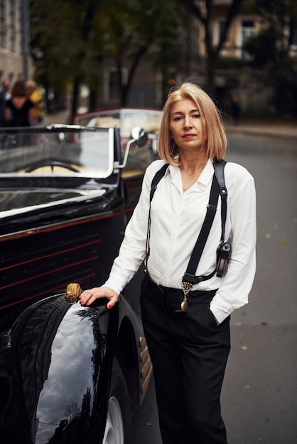 Mujer rubia en ropa negra cerca viejo coche clásico vintage. | Foto Premium