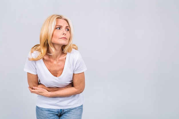 Mujer rubia senior madura en casual con dolor de estómago aislado en un fondo blanco gris. Fuerte dolor de estómago.