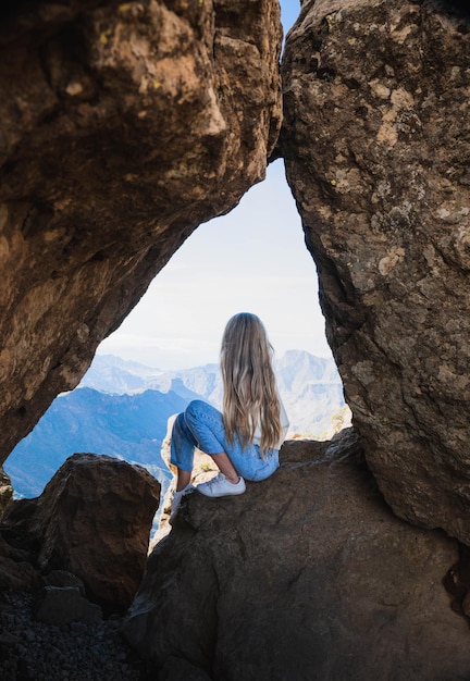 Mujer rubia sentada en una roca con la increíble vista del Roque Nublo en Gran Canaria