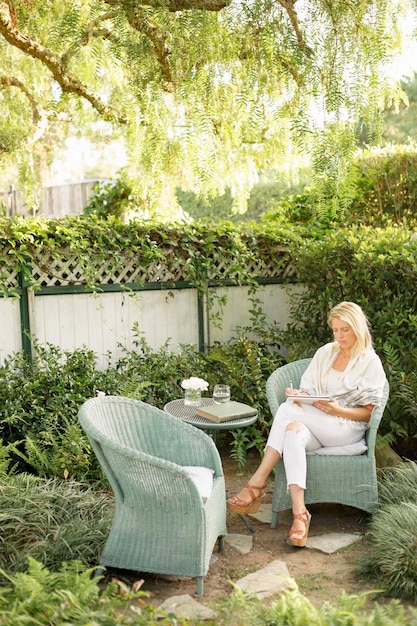 Mujer rubia sentada en una silla de mimbre en un jardín.