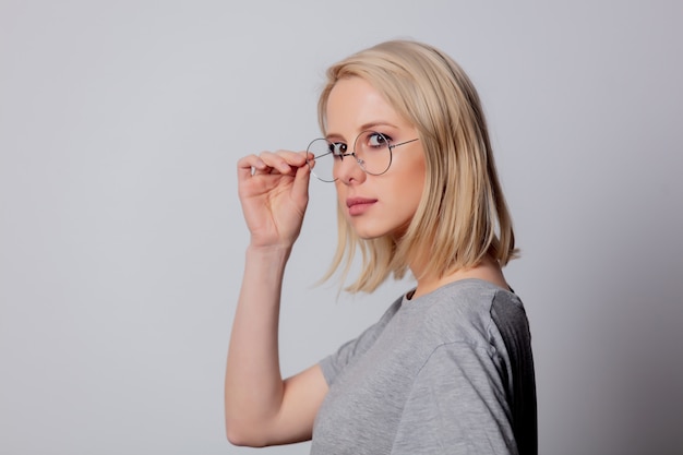 Mujer rubia seria en vidrios en la pared blanca